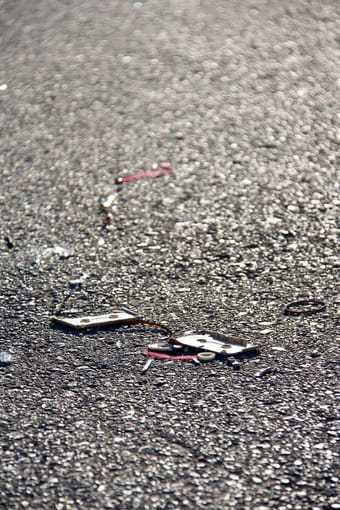 A broken cassette and loose tape lie on sunlit asphalt.