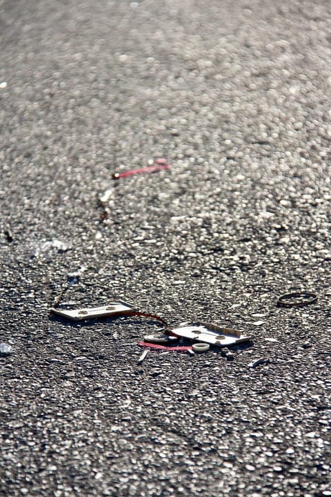 A broken cassette and loose tape lie on sunlit asphalt.